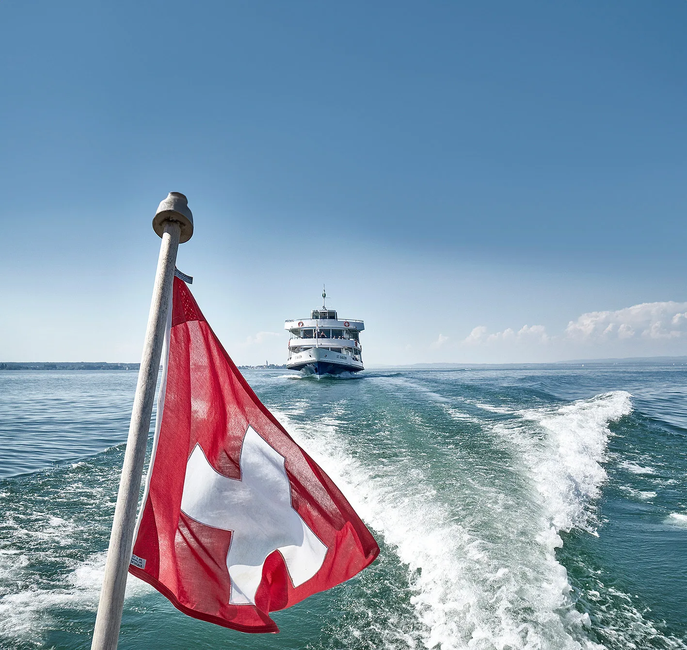 Schweizer Flagge am Heck mit Schiff im Kielwasser.